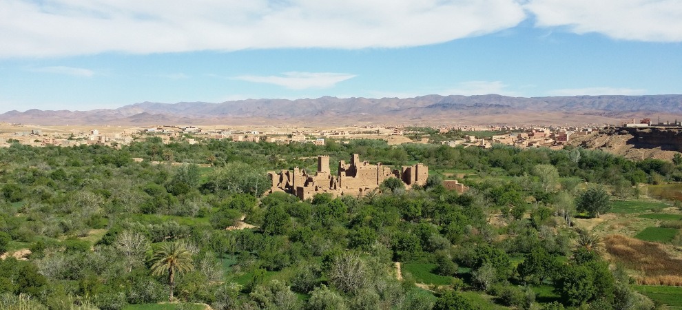 view of kasbah in green valley with mountains in background, at Kalaat M'Gouna (Valley of the Roses)