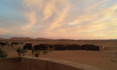 traditional nomad tents in bivouac against backdrop of big dunes and pretty sunset clouds