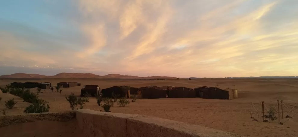 traditional nomad tents in bivouac against backdrop of big dunes and pretty sunset clouds