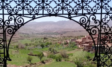 view of green valley through arched ironwork window opening at Telouet Kasbah