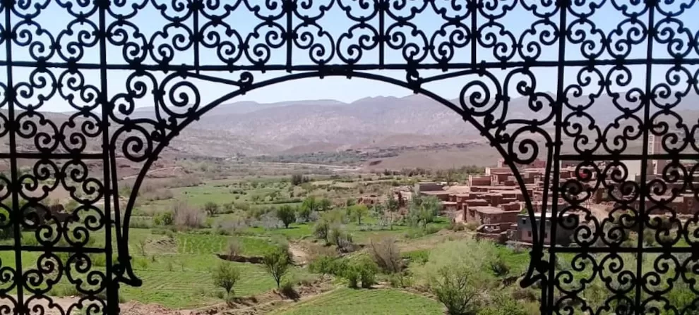 view of green valley through arched ironwork window opening at Telouet Kasbah