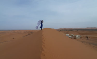 bedouin man standing on top of dune, white scarf blowing in the wind, big dunes in background