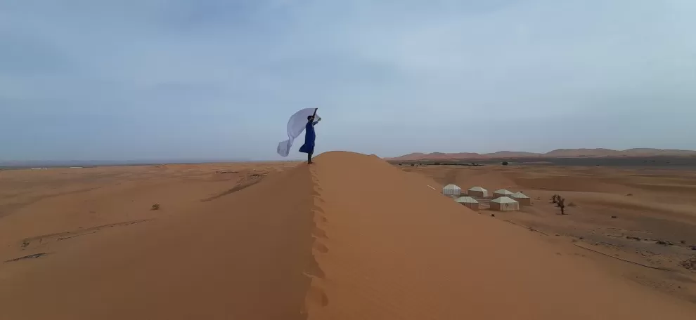 bedouin man standing on top of dune, white scarf blowing in the wind, big dunes in background