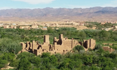 panoramic view overlooking Kalaat M'Gouna "Valley of the Roses", showing green valley with Kasbah ruins in the centre, Atlas Mountains in the far distance