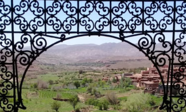 view of green valley and mountains through arched ironwork window at Telouet Kasbah