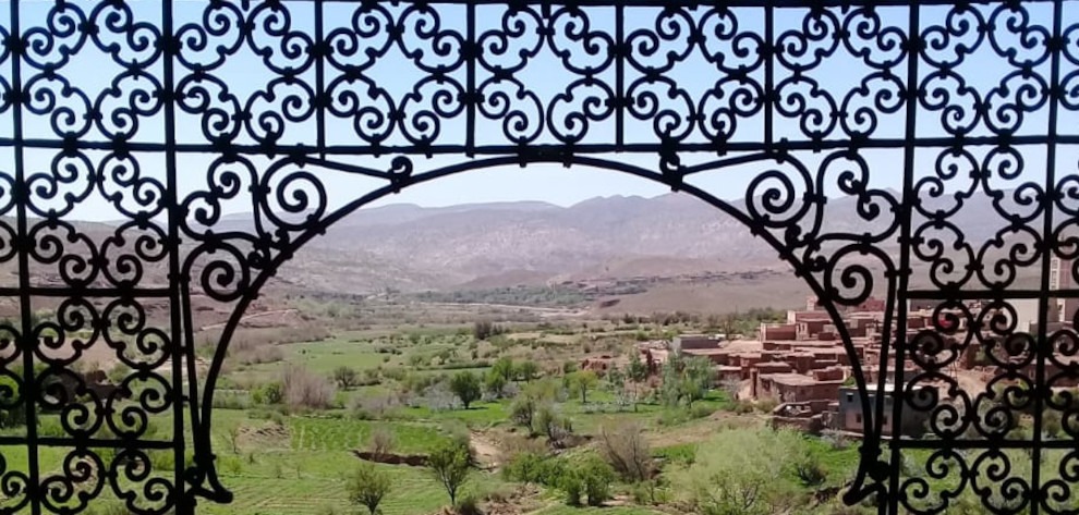 view of green valley and mountains through arched ironwork window at Telouet Kasbah