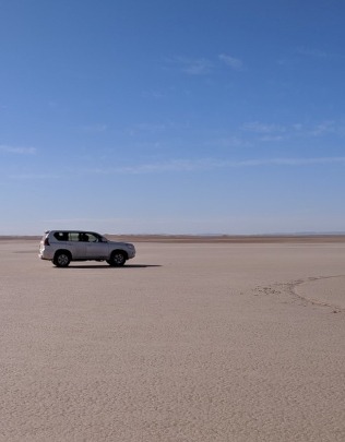 Lake Iriki- vehicle parked on flat, dry lakebed in southern Morocco, bright blue sky